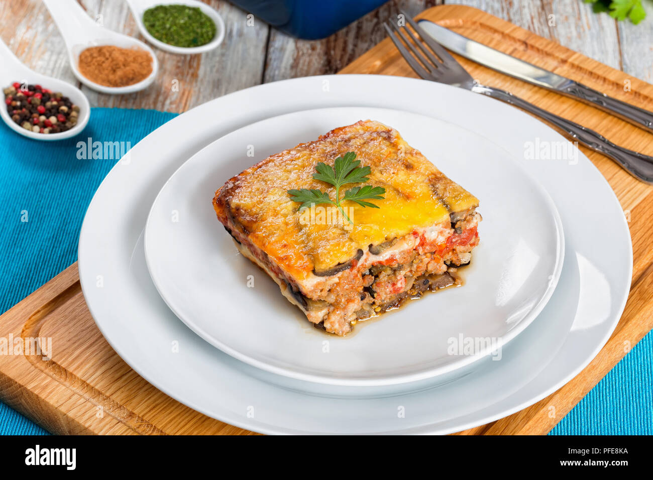 Teil der Köstlichen layered Moussaka mit Petersilie für authentische Rezept gekocht dekoriert, mit Petersilie auf Teller mit Messer und Gabel eingerichtet, auf whi Stockfoto