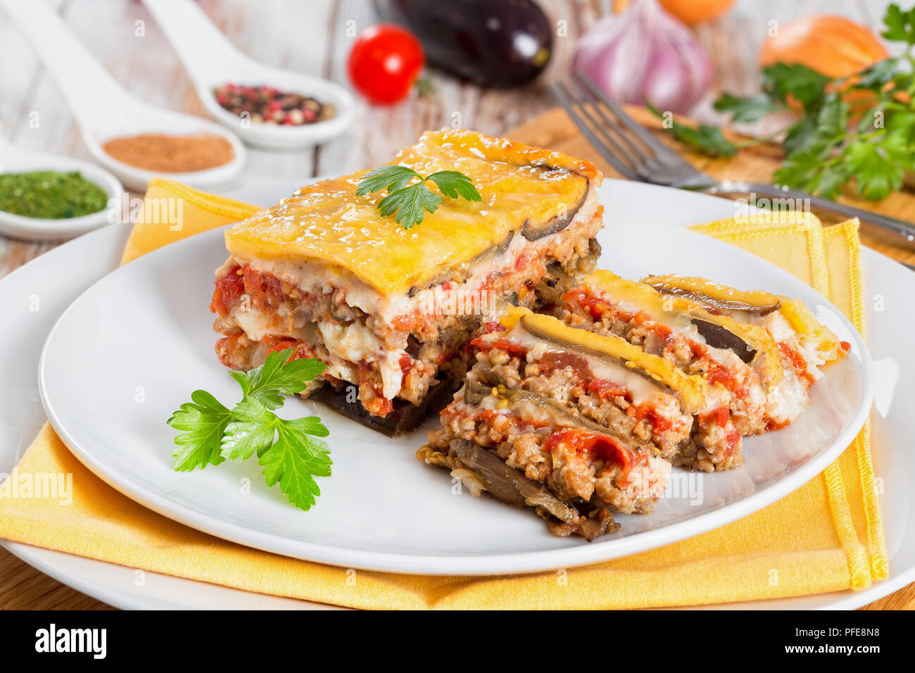 Teil der Köstlichen layered Moussaka mit Petersilie in Scheiben für authentische Rezept gekocht Schneiden eingerichtet, auf Platten mit Serviette, auf weissem Peeling pa Stockfoto