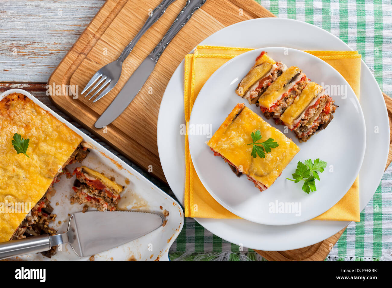 Teil der Köstlichen layered Moussaka mit Petersilie in Scheiben für authentische Rezept gekocht Schneiden eingerichtet, auf Platten mit Serviette und in der auflaufform, Stockfoto