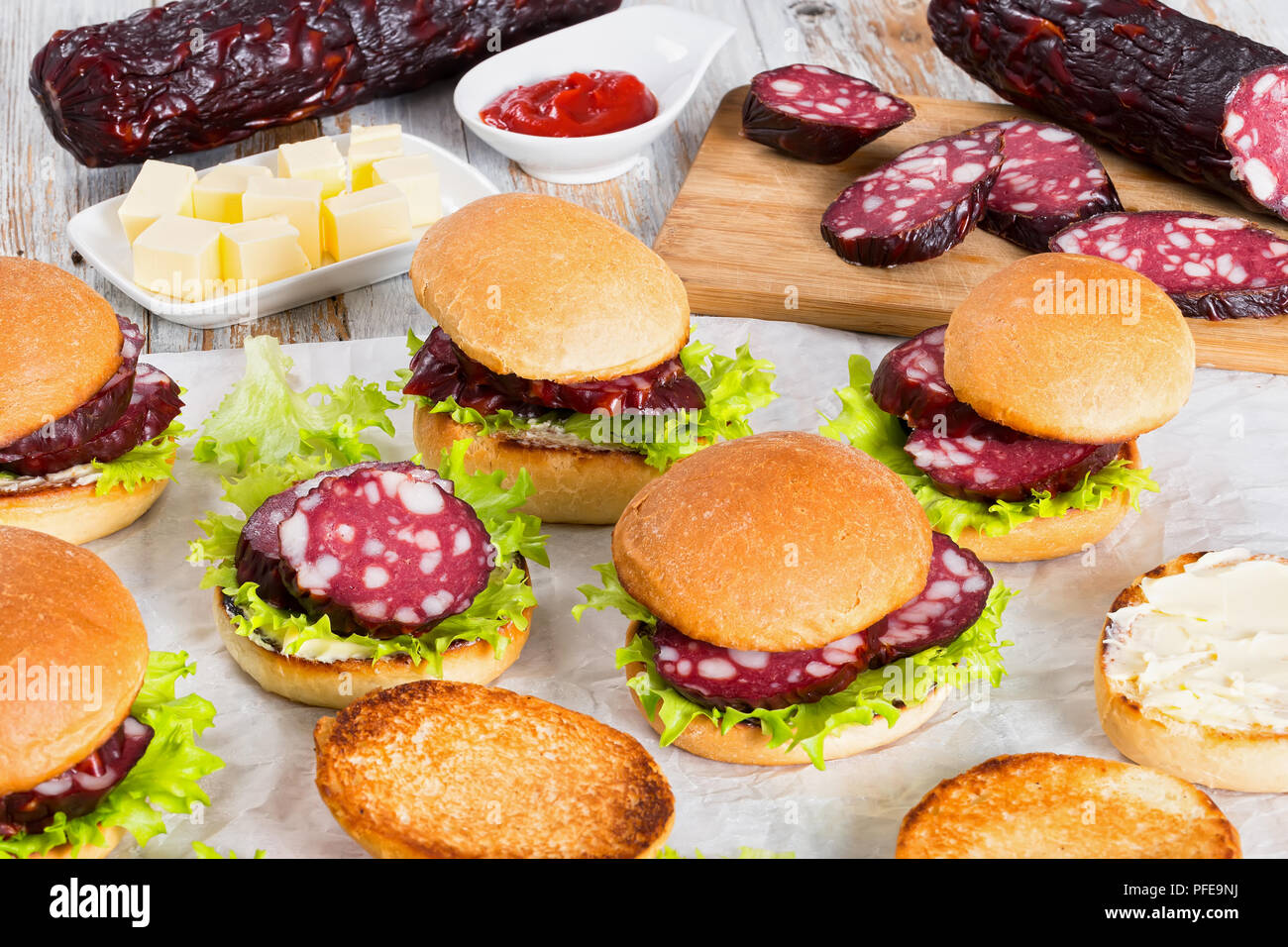 Köstliche Sandwiches mit Butter, Salat und Scheiben geräucherte Wurst in gebratene Brötchen auf weißem Pergamentpapier, Butter Würfel, Barbecue Sauce und Stockfoto