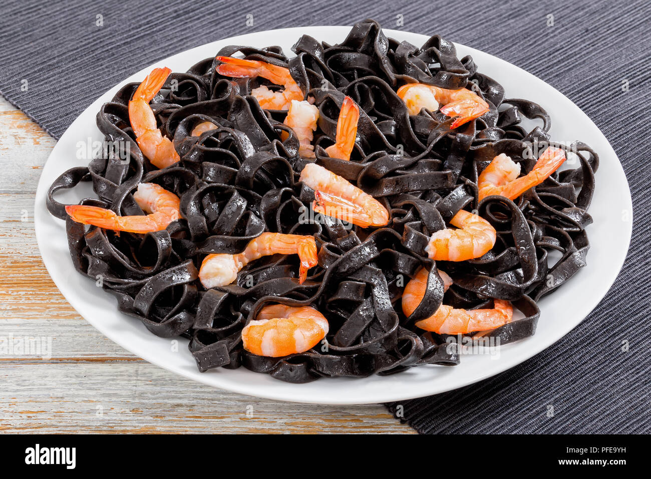 Tintenfisch schwarze Nudeln mit Garnelen auf weißem platter auf dunklen Tisch Matte auf alten Holztisch, Nahaufnahme, Ansicht von oben Stockfoto