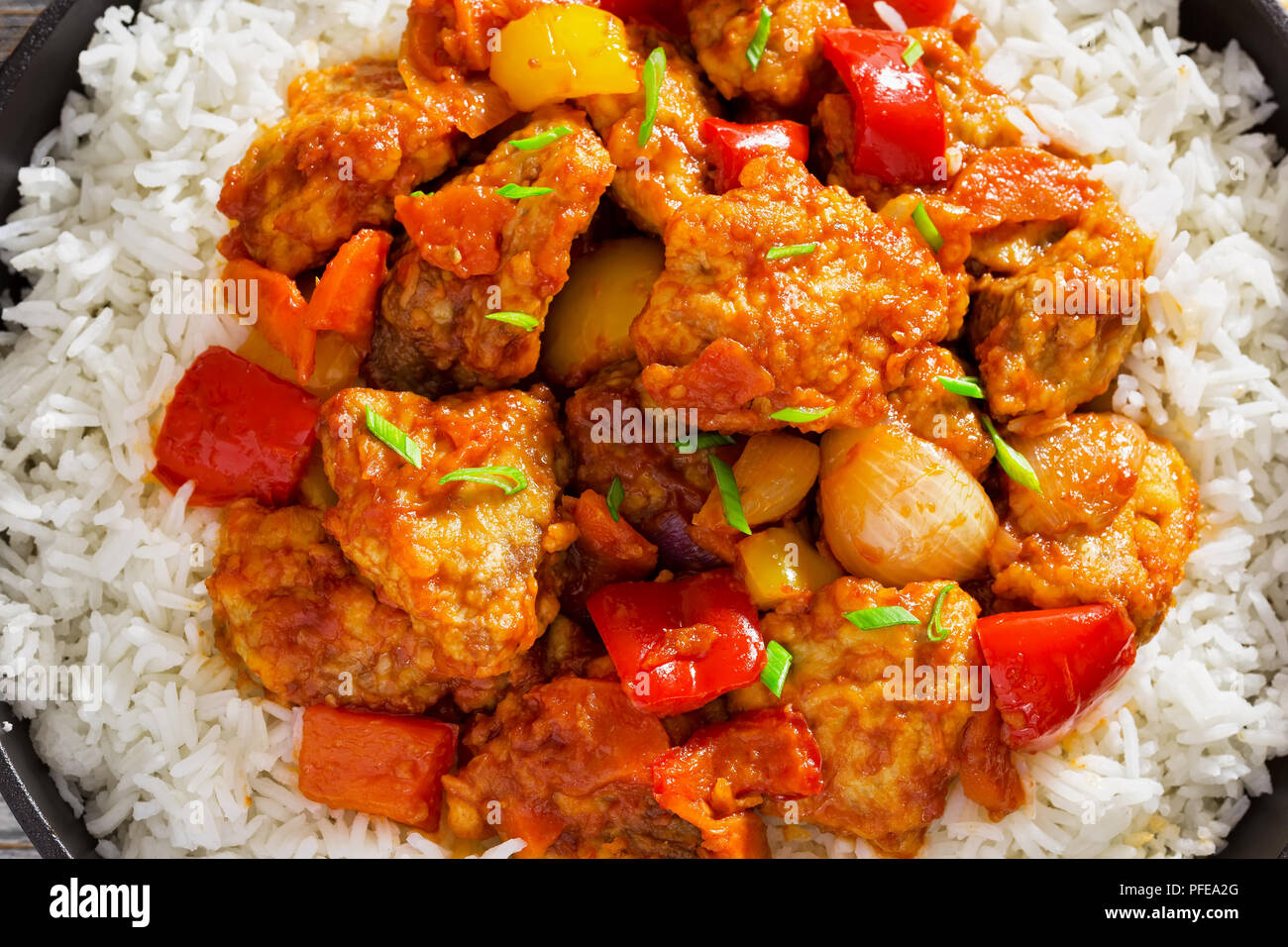 Reis und süß und sauer gebratenes Schweinefleisch Chunks mit Paprika, Zwiebeln, Ananas und Tomatensauce bestreut mit Frühlingszwiebeln in Eisen stewpan auf weißem Plan Stockfoto