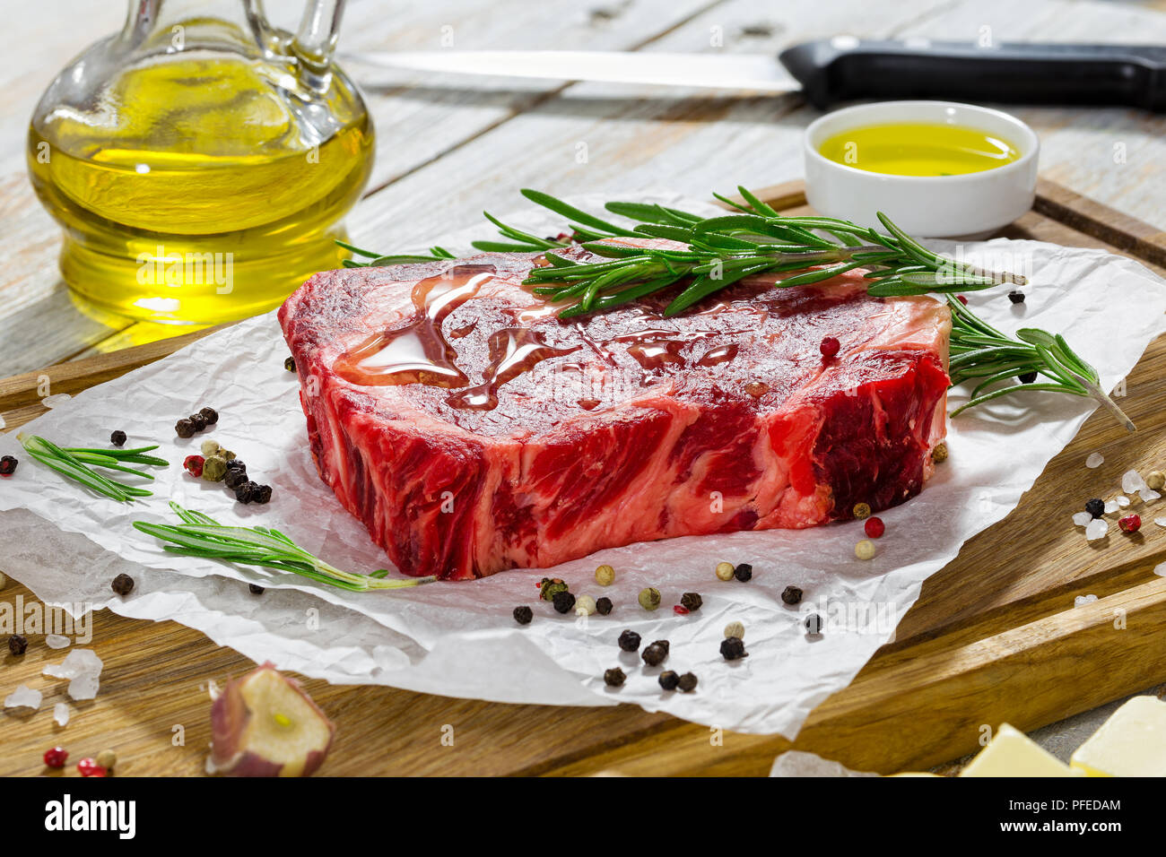 Rohes Rindfleisch Rib Eye frisches Fleisch Steak auf weißem Papier auf Schneidebrett mit Rosmarin gegossen mit Olivenöl, Knoblauch, koscheres Salz, Butter und Olivenöl Stockfoto