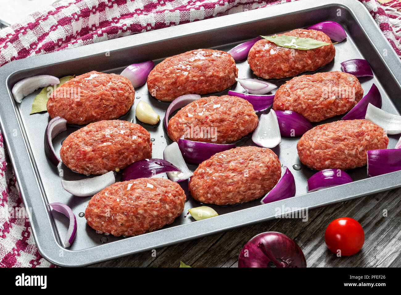Frischem Boden rohes Fleisch Koteletts mit roten Zwiebeln, Knoblauch und Lorbeer beträufelt mit Olivenöl in Auflaufform mit Küchentuch, Ansicht von oben, Schließen - Stockfoto