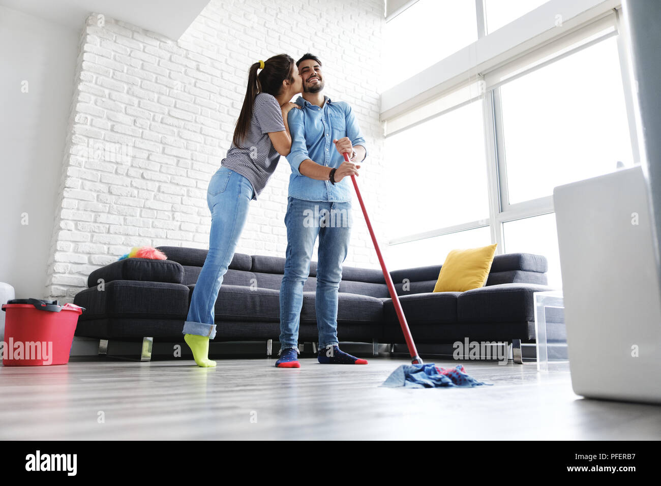 Junges Paar, Hausarbeit und Hausarbeiten. Mann und Freundin wischt den Boden mit Mop. Fühlt sich die Frau stolz auf ihren Mann und küsst ihn. Stockfoto