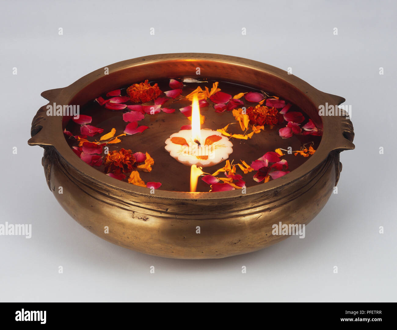 Schwimmende Kerze und Blütenblätter in Messing Schale mit Wasser. Stockfoto