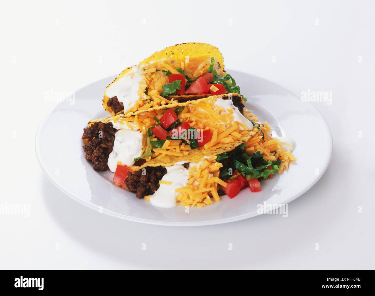 Tacos gefüllt mit Sauerrahm, Käse, Salat und Hackfleisch, auf einer Platte Stockfoto