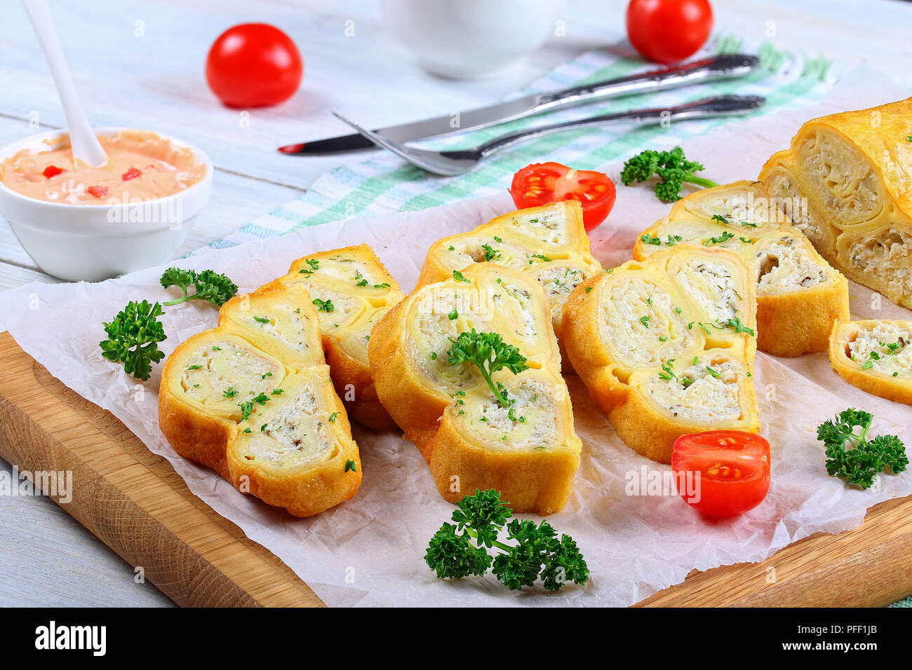 Crepes Brötchen mit gehacktem Hühnerfleisch, Cottage und Kräuter in Scheiben schneiden auf Schneidebrett mit frischer Petersilie und Tomaten, Gabel, Messer, gefüllt, s Stockfoto