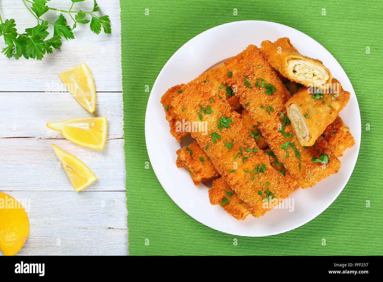 Lecker Knusprig paniert Gebackene Hackfleisch Huhn Enchiladas roll-ups ganz und halbiert auf weiße Platte, Zitronenscheiben und Petersilie auf Holz- Tabelle, Ansicht Stockfoto