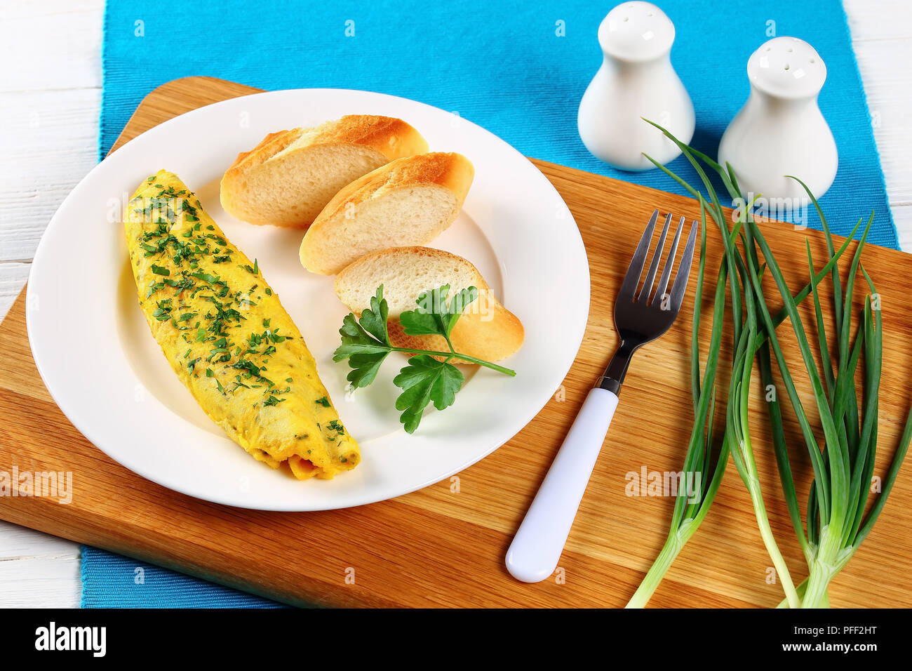 Köstliche französische Ausschreibung Omelette serviert auf weiße Platte mit Baguette Scheiben und frische Petersilie auf Schneidebrett mit Salz- und Pfefferstreuer und Feder Stockfoto