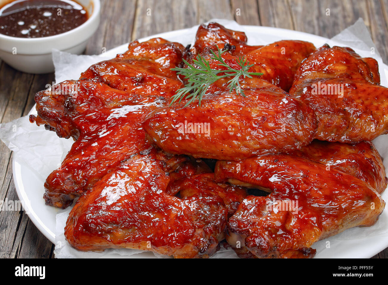 In der Nähe von köstlichen Honig Knoblauch Ingwer Chicken Wings auf Platte auf dunklen Holztisch mit Barbecue Sauce auf den Hintergrund, Ansicht von oben Stockfoto