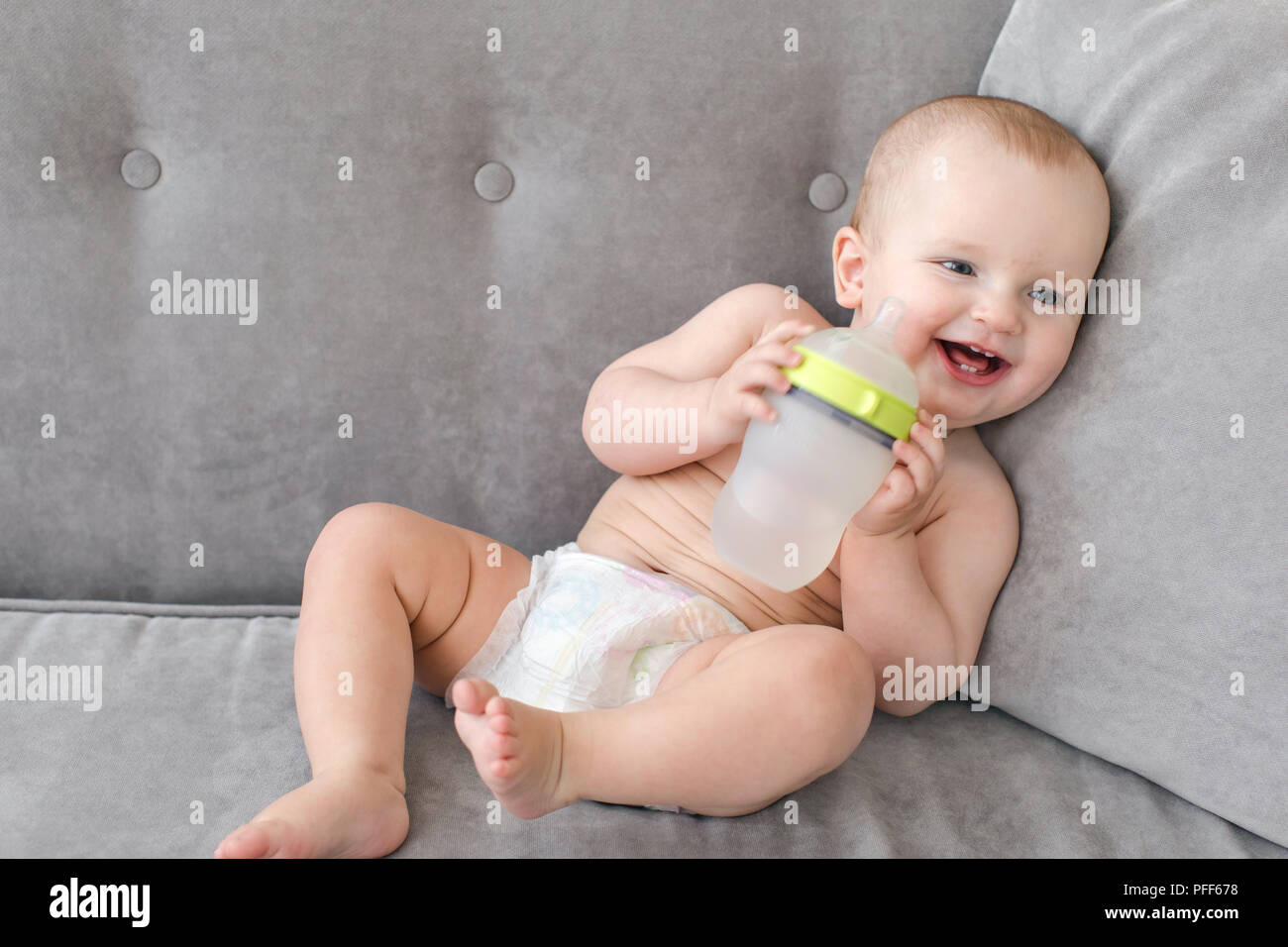 Fröhliches Baby mit Flasche auf dem Sofa Stockfoto
