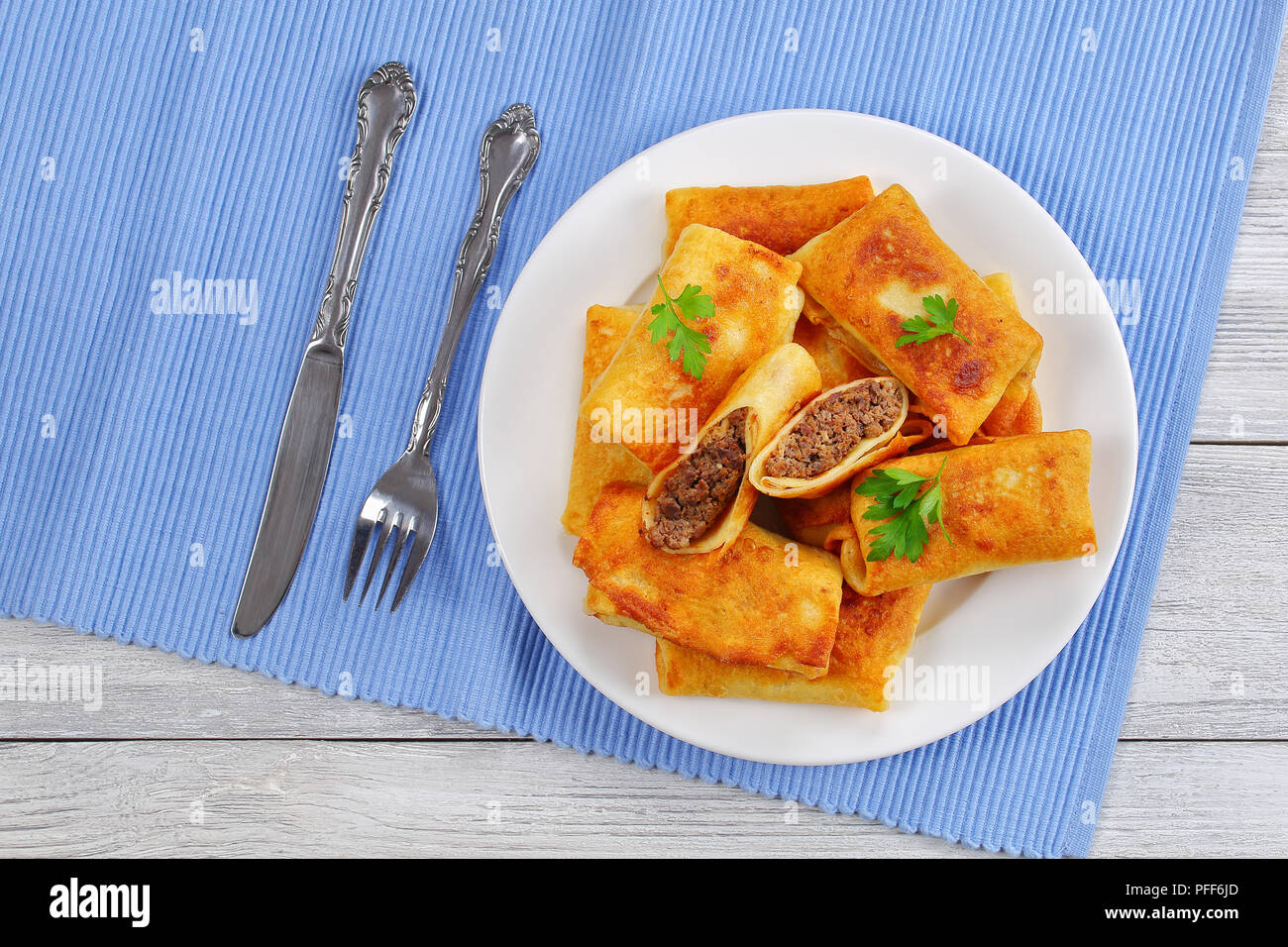 Aufgerollt köstliche Crêpes mit Hackfleisch/Leber auf weißem Schild auf alten hölzernen Tisch mit Messer und Gabel auf den Tisch matte gefüllt, Ansicht von oben Stockfoto