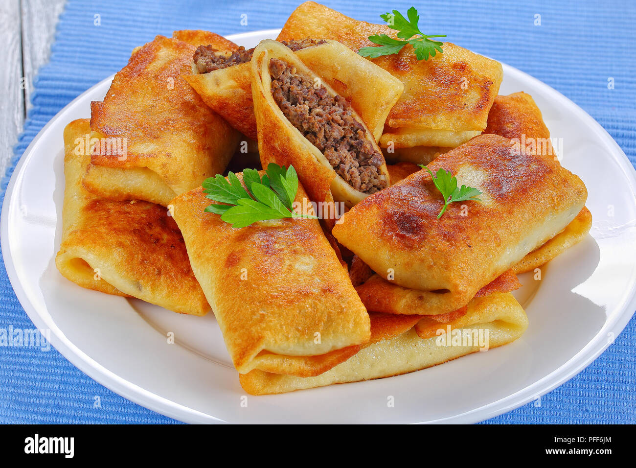 Aufgerollt köstliche Crêpes mit Hackfleisch/Leber und Fleisch auf weiße Platte auf alten Holztisch mit Messer und Gabel auf den Tisch matte gefüllt, Ansicht von oben, Cl Stockfoto