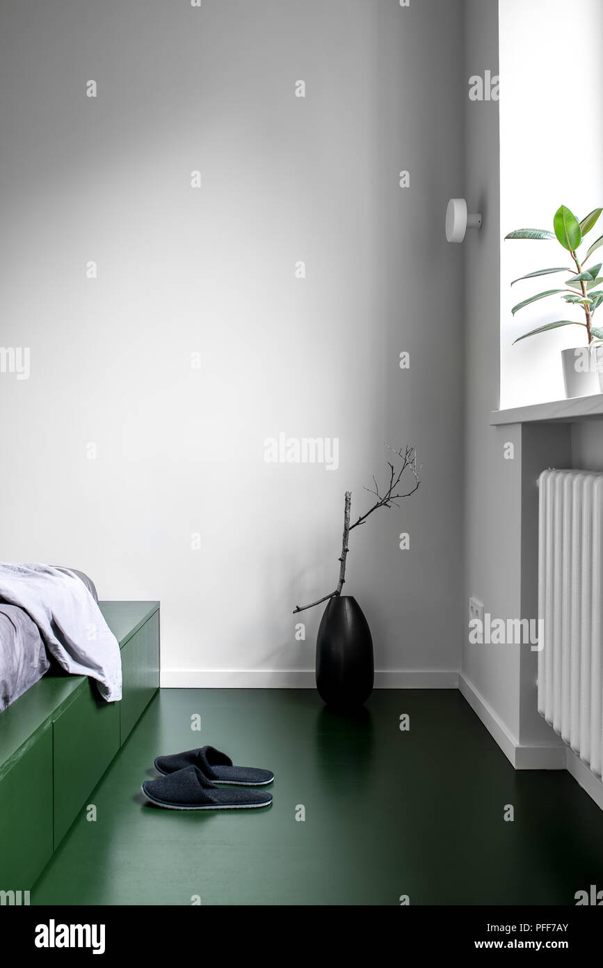 Trendy Schlafzimmer im modernen Stil mit weißen Wänden und grünen Boden. Es ist ein grünes Bett mit Schubladen und pastellfarbene Bettwäsche, schwarz Vase mit einem Zweig, gree Stockfoto