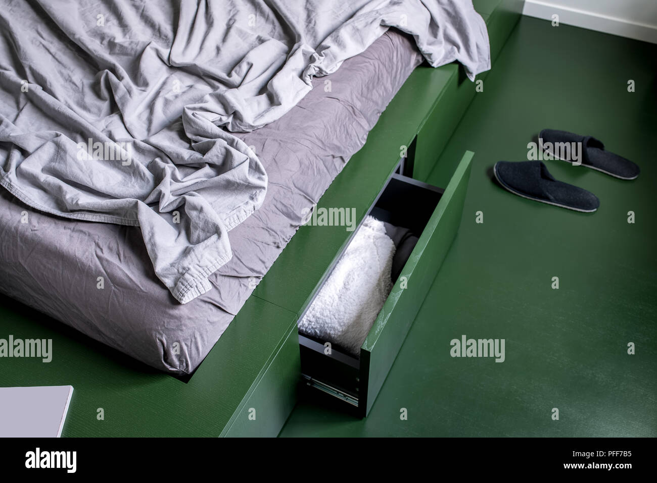 Stilvolle Zimmer in einem modernen Stil mit weißen Wänden und grünen Boden. Es ist ein grünes Bett mit Schubladen und pastellfarbene Bettwäsche, schwarz Hausschuhe auf dem Boden. C Stockfoto