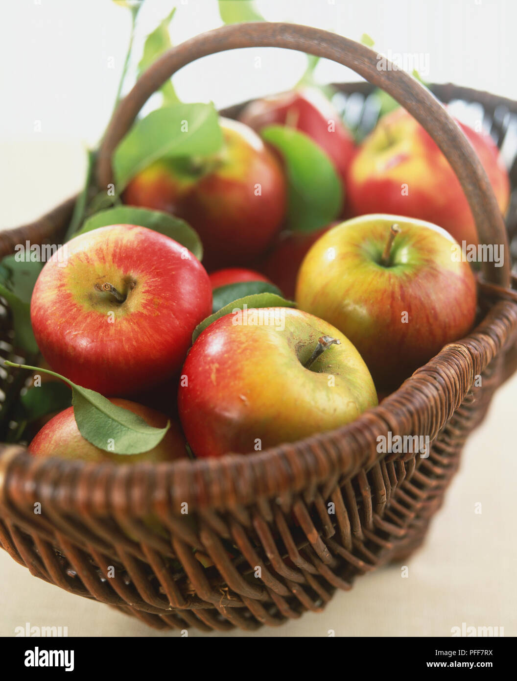 Rote und grüne Äpfel im Strohkorb mit Griff, Vorderansicht. Stockfoto