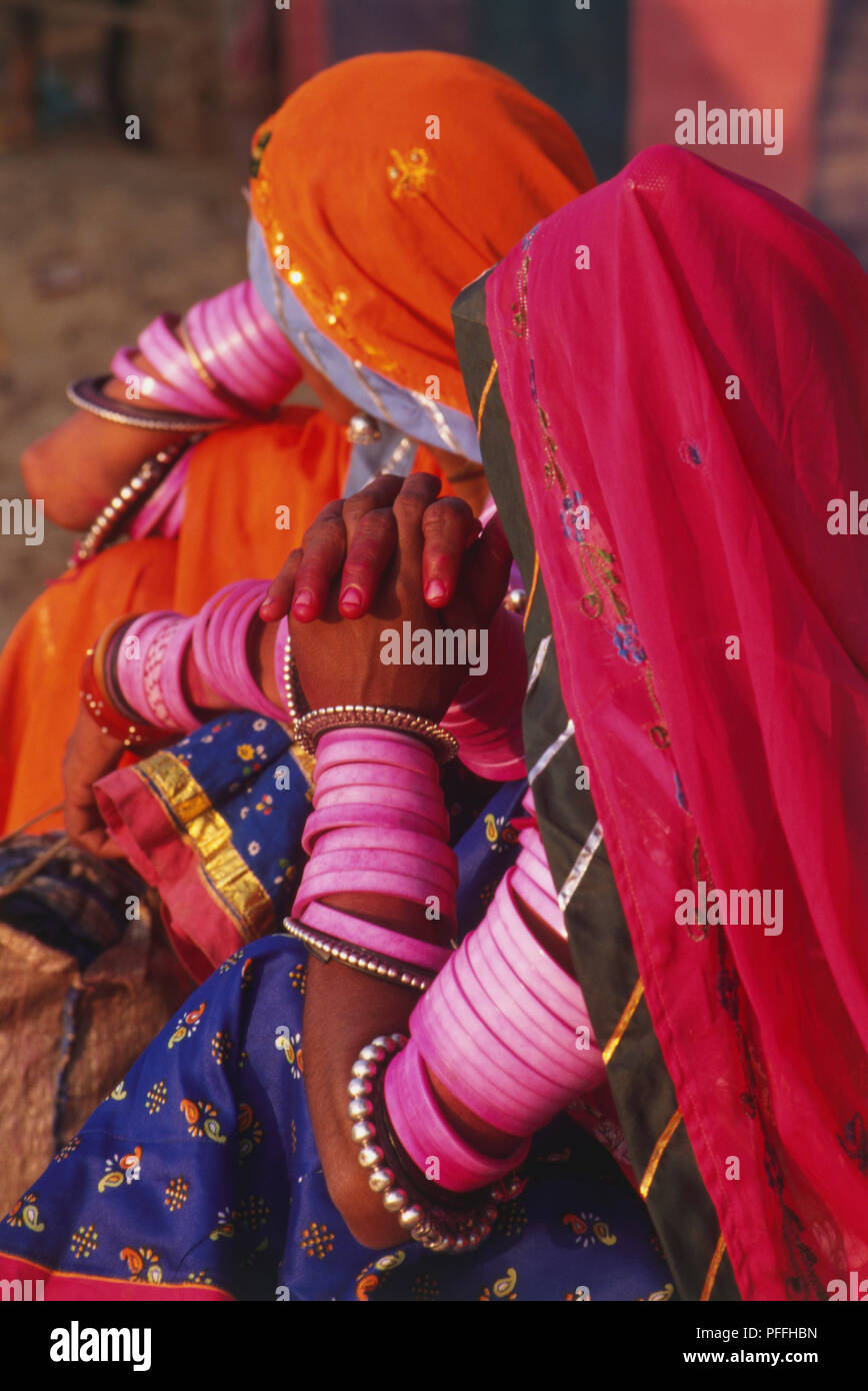 Indien, Frauen tragen traditionelle indische Kleid, pink und orange ghunghat Schleier über ihre Gesichter, viele Rosa Armreifen der Handgelenke und Oberarme. Stockfoto