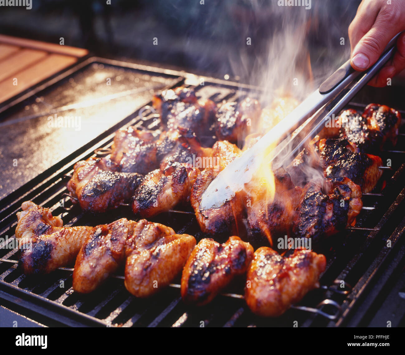 In der Nähe von Metall skwers remving ein Honig Soja Chicken Wings aus der brennenden Grill. Stockfoto