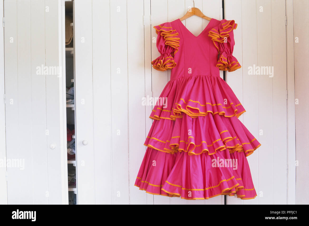 Frilly und Flouncy flamenco Kleid (Trajes Flamencas) hängen an der vorderen Tür eines weißen Holzschrank. Stockfoto