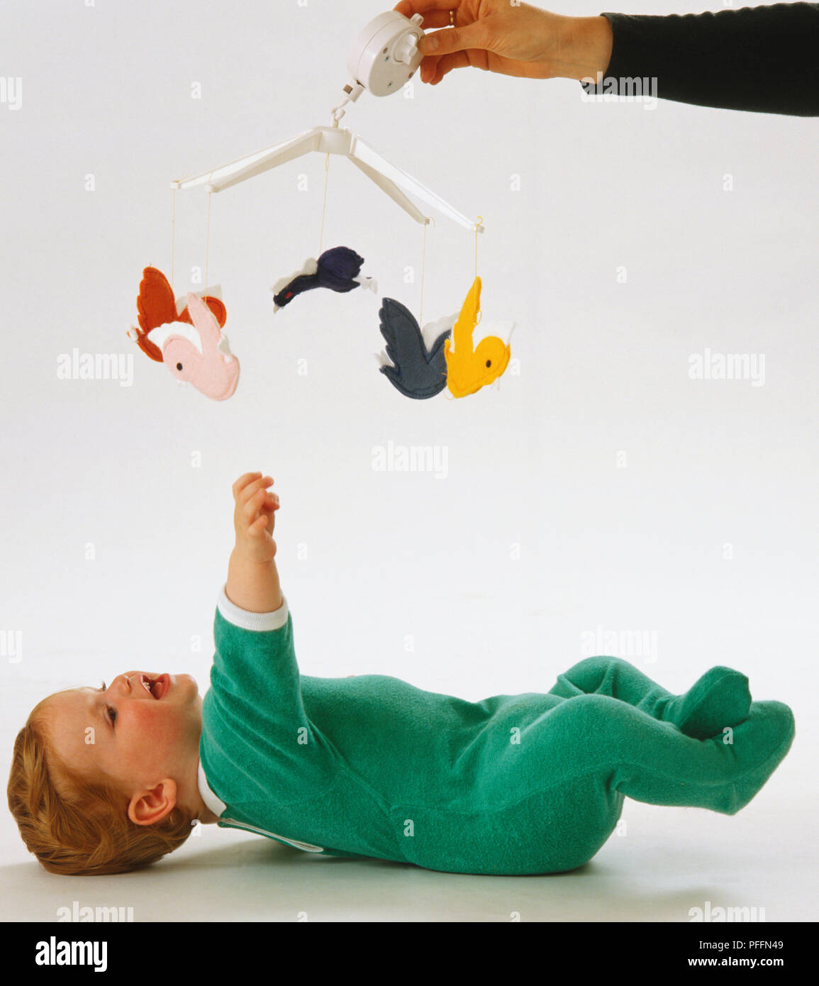 Baby Tragen von grünen Overall, der lag auf dem Rücken, Beine in die Luft, packte für bunten Spielzeug mobile, aufgeregt. Stockfoto