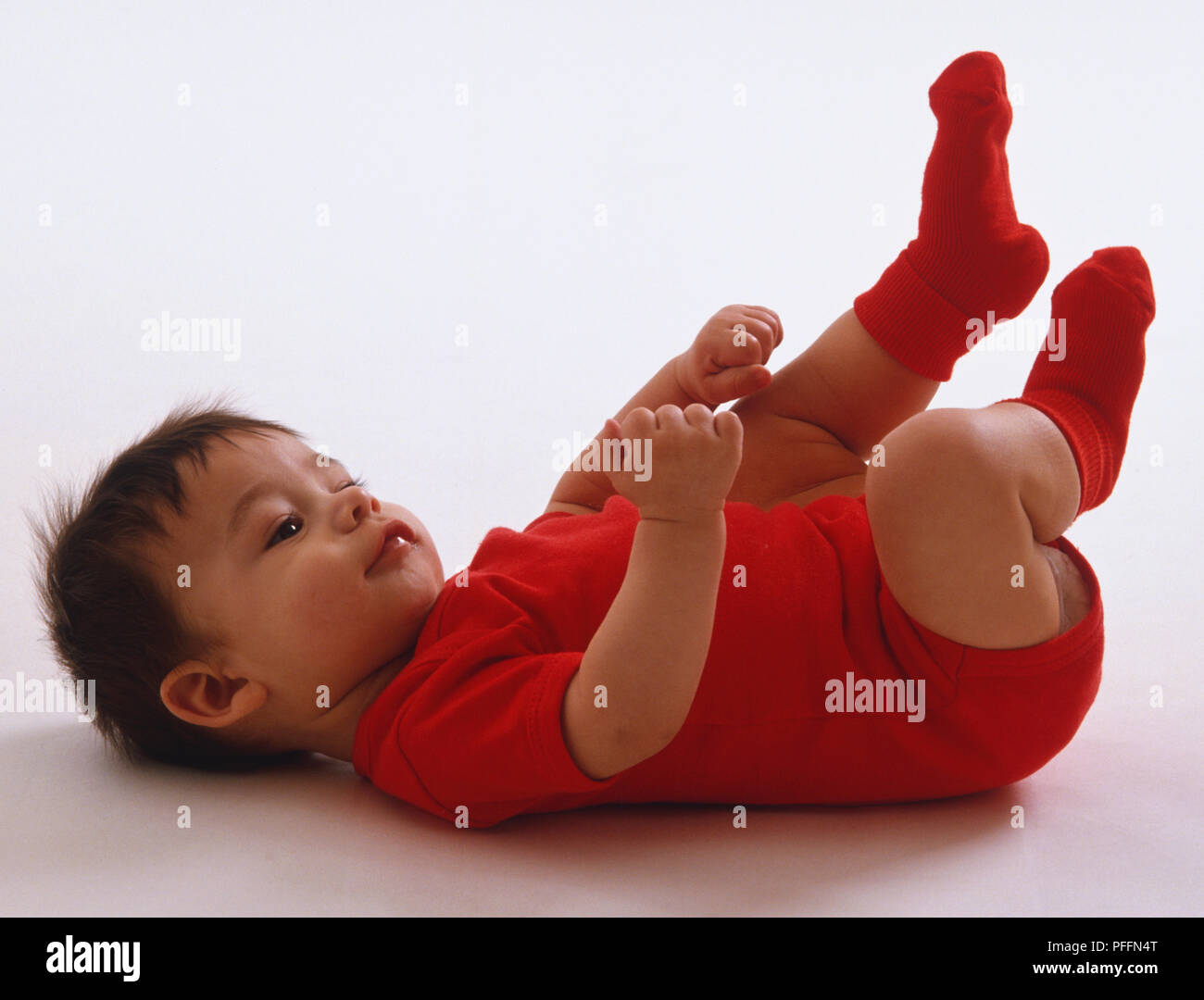 Baby das Tragen der roten Overall und Socken, Lügen auf Zurück, treten die Füße in die Luft, amüsiert, Seitenansicht. Stockfoto