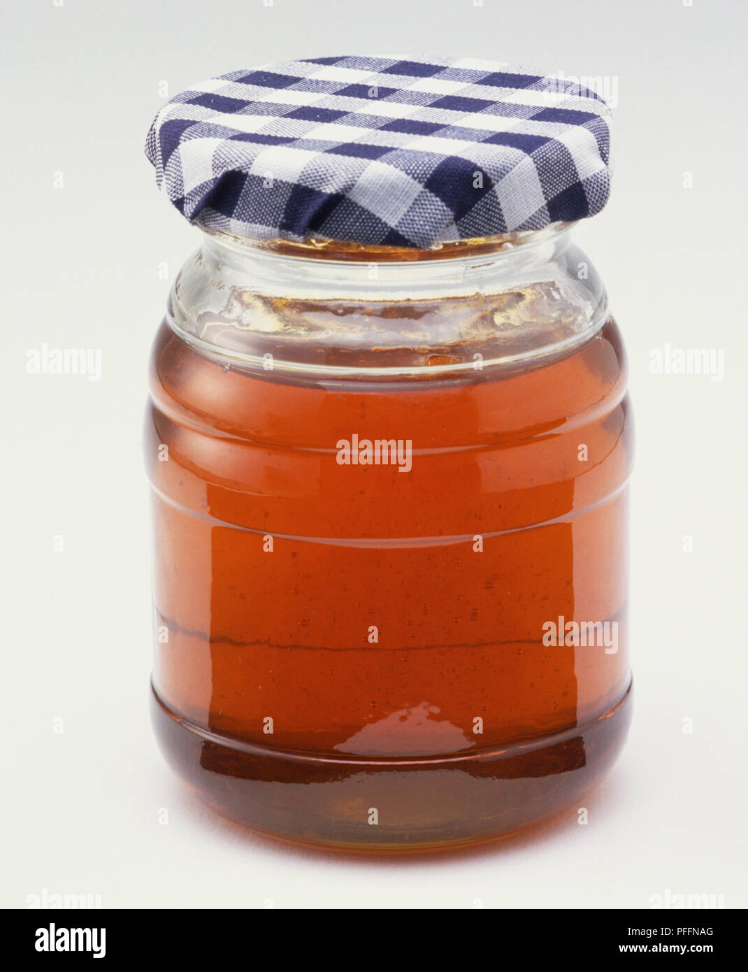 Kleines Glas Honig mit einem karierten Deckel. Stockfoto
