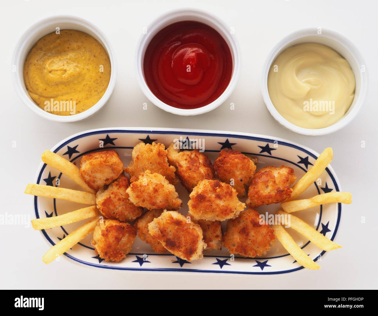 Oben Ansicht von Chicken Nuggets, gemacht mit Huhn beschichtet in breadcrumb Teig, auf Fach, mit Pommes mit Ketchup, Mayonnaise und Senf zum Dippen. Stockfoto