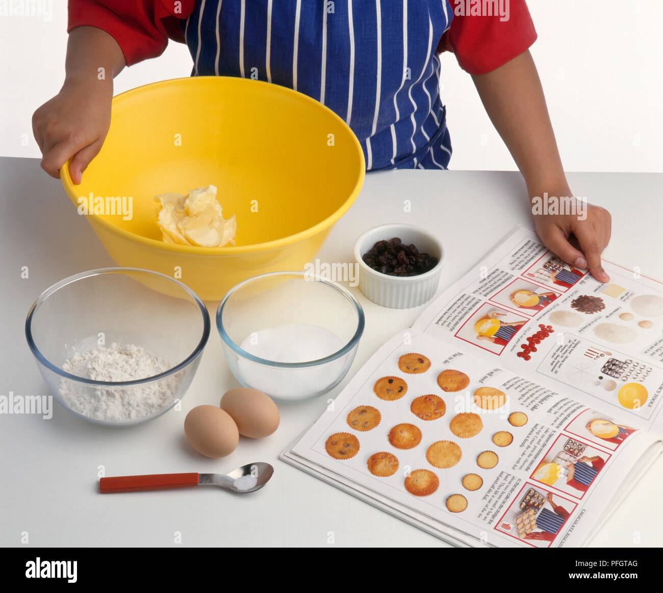 Boy's Hand an Zutaten in der Küche Buch zeigt, Schüssel Butter, Schalen von Mehl und Zucker, Eier in der Nähe Stockfoto