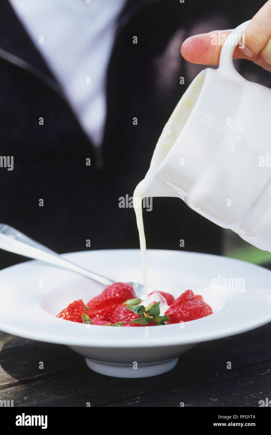 Pudding aus weissen Krug über Schüssel mit frischen Erdbeeren, Seitenansicht. Stockfoto