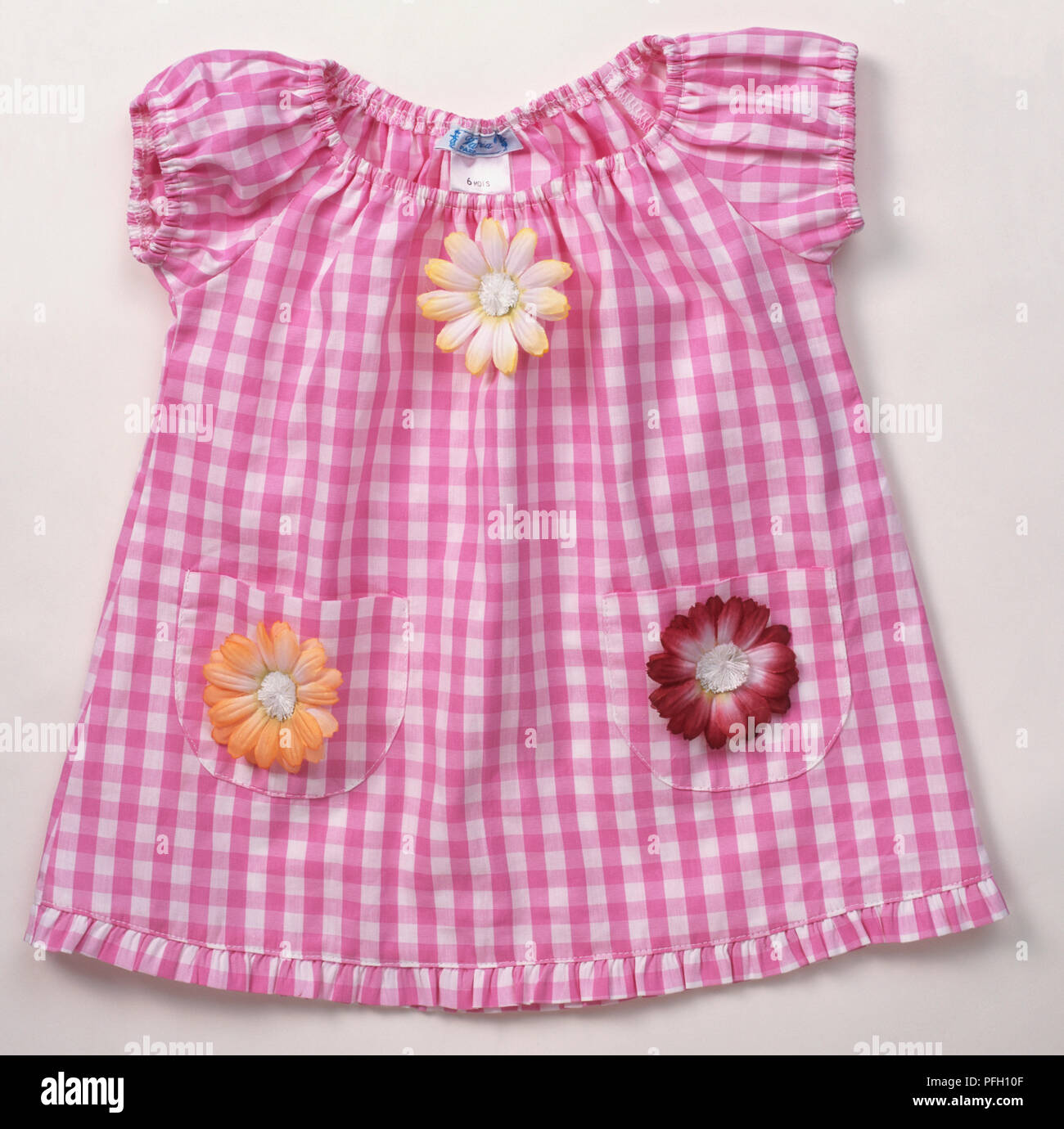 Rosa und Weiß kariertem Stoff baby Kleid mit Blumen an den Taschen und Brust, elastische Bündchen an Ärmeln und Ausschnitt. Stockfoto