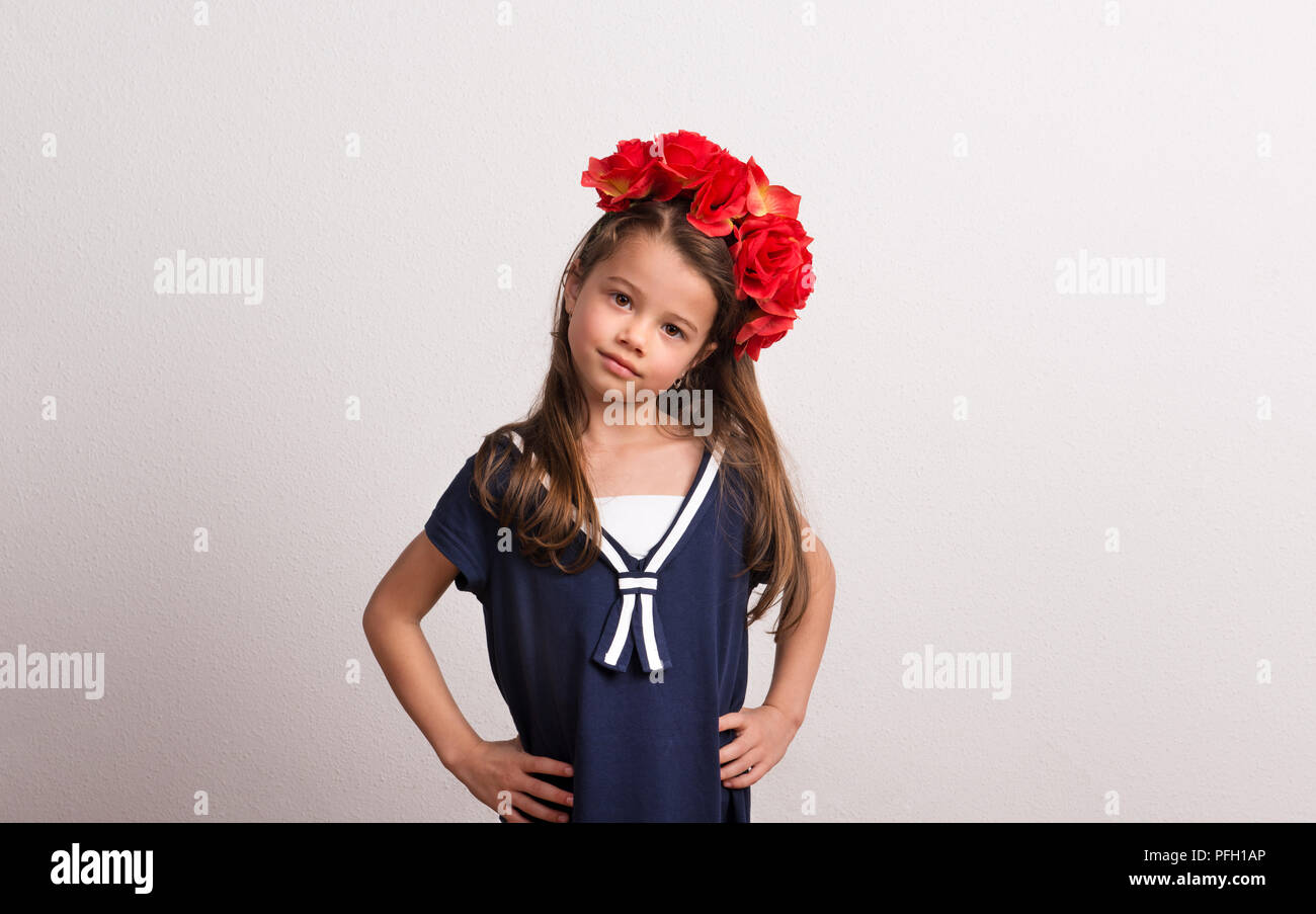 Porträt von einem kleinen Mädchen mit Blume Kopfband, die Arme in die Hüften. Ein studio shot auf einem weißen Hintergrund. Kopieren Sie Platz. Stockfoto