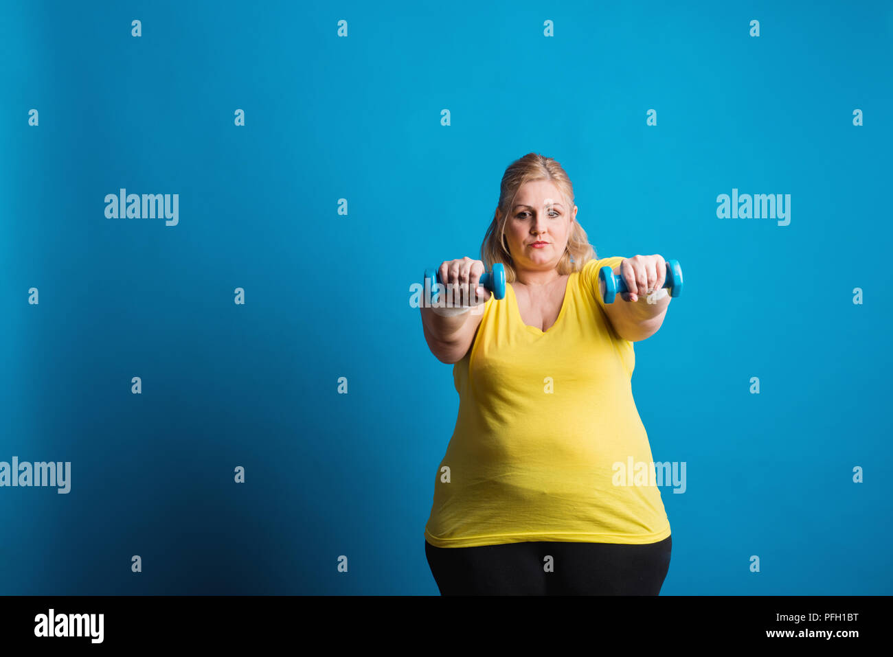 Portrait eines unglücklichen übergewichtige Frau mit Hanteln in den Händen. Studio shot auf blauem Hintergrund. Kopieren Sie Platz. Stockfoto