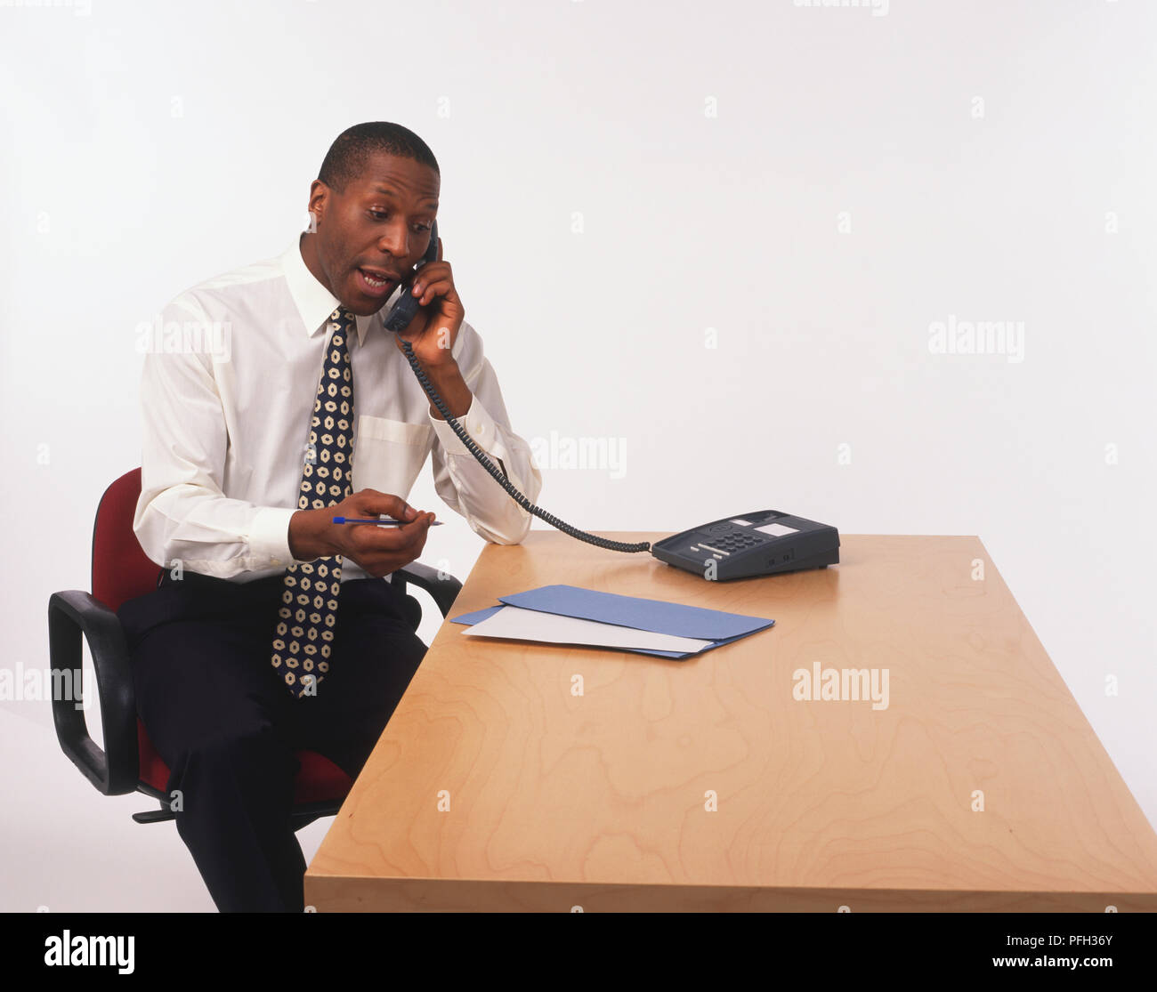 Mann im weißen Hemd und am Schreibtisch, am Telefon zu sprechen und die Feder sitzt Riegel Stockfoto