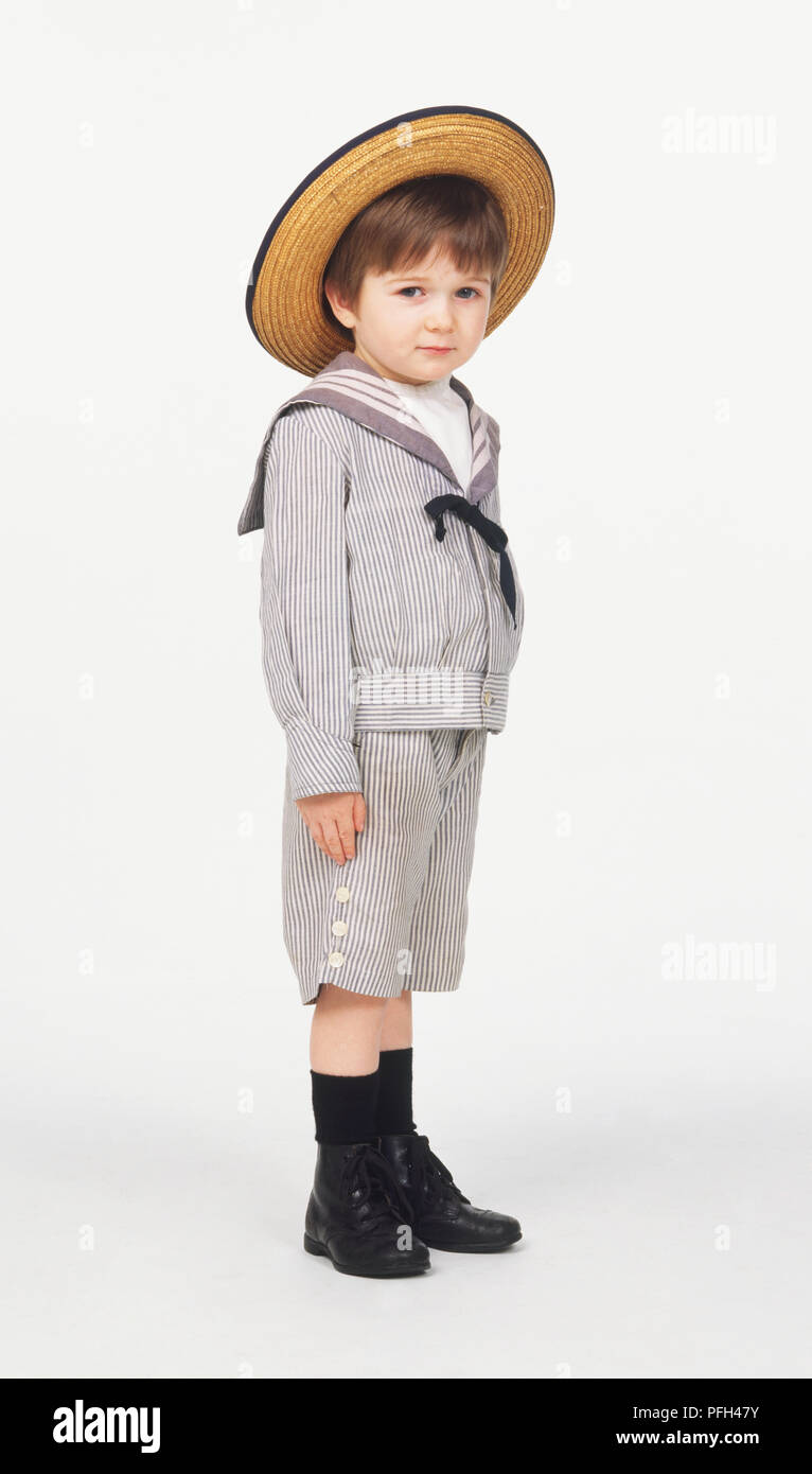 Seitenansicht eines Jungen im Matrosenanzug und Strohhut, mit Blick auf die Kamera Stockfoto