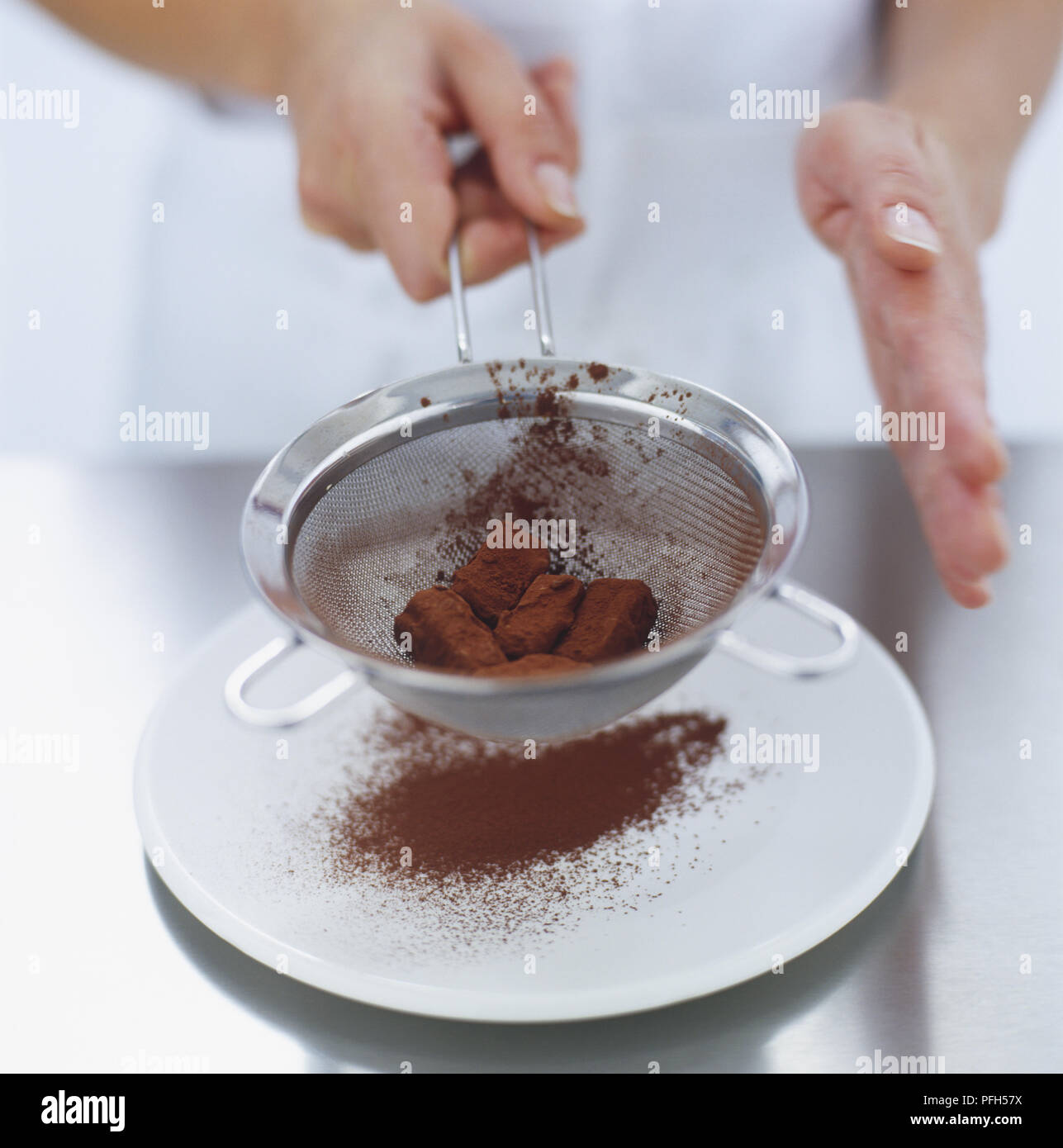 Überschüssige Kakaopulver wird abgeschüttelt Schokolade Trüffel in einem Sieb Stockfoto