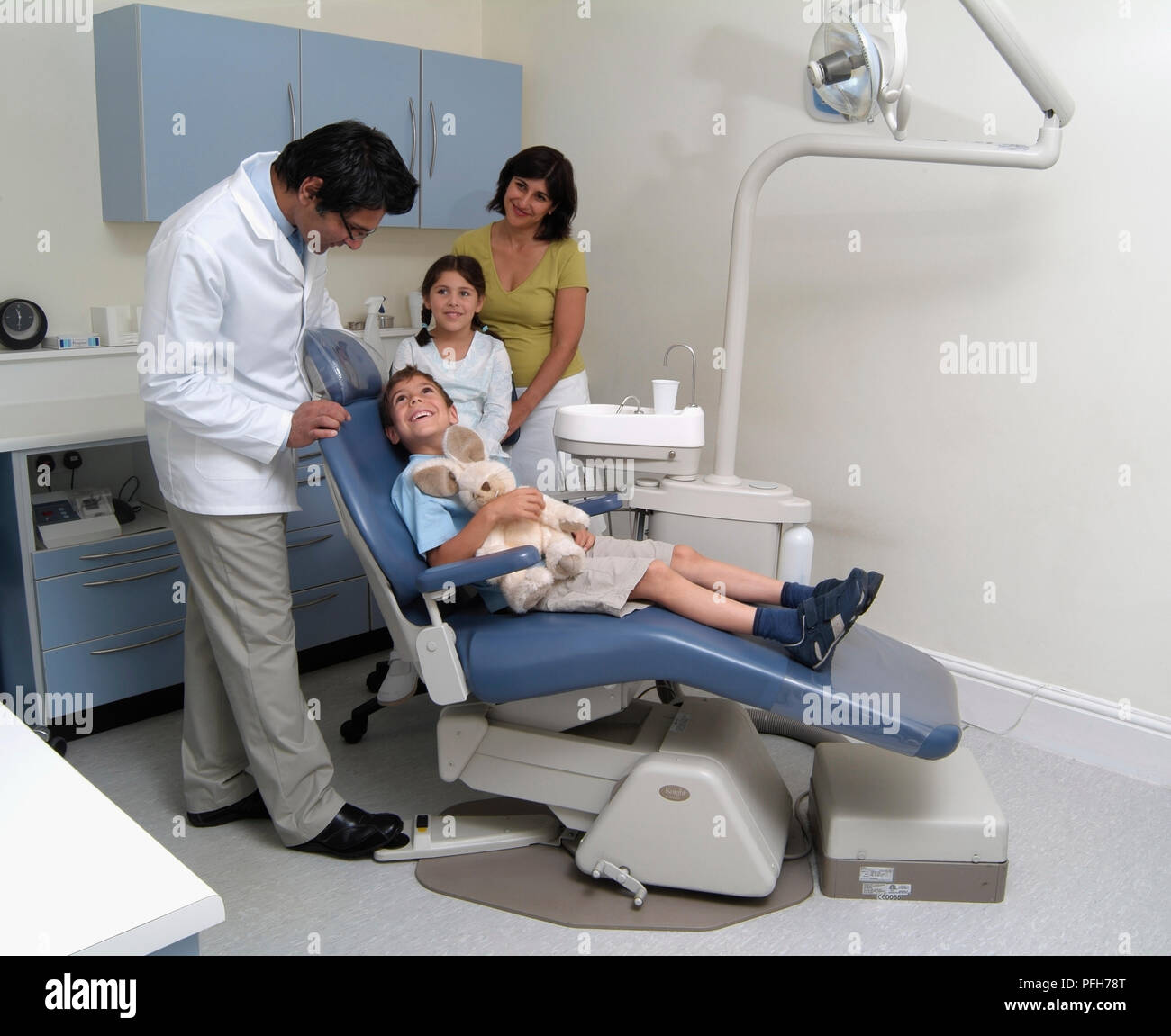 Junge in den Zahnarztstuhl zu Zahnarzt, Frau und Mädchen im Hintergrund Stockfoto