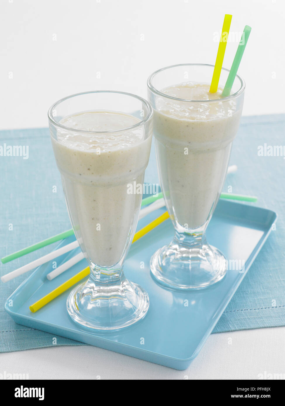 Ananas Milchshakes serviert in hohe Gläser mit bunten Trinkhalmen auf Blau Fach Stockfoto
