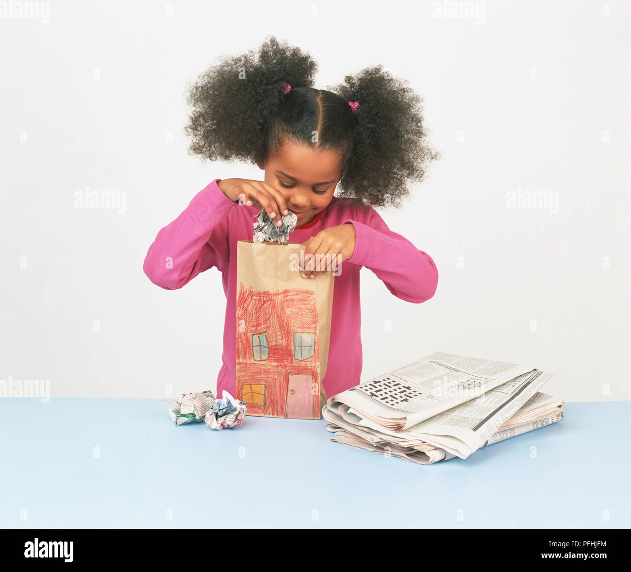 Mädchen mit Pigtails, kniff die Zeitung in einer Papiertüte mit einer Zeichnung von einem Haus auf der Vorderseite, Ordner Zeitung neben. Stockfoto