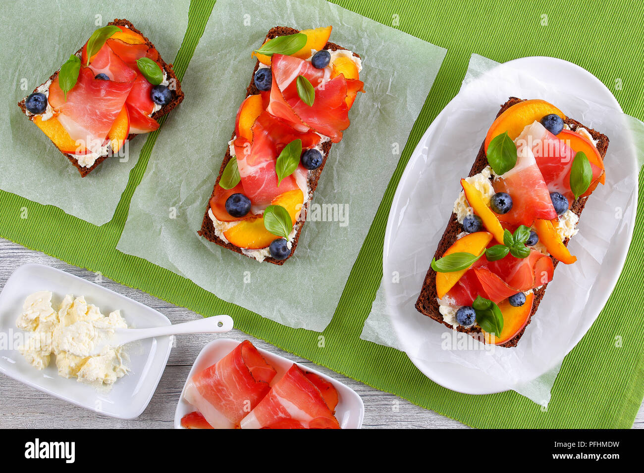 Leckere bunte Sandwiches mit Frischkäse, Blaubeeren, Pfirsich, Schinken Scheiben und Blätter Basilikum auf Roggenbrot mit Zutaten aus Holz- t Stockfoto