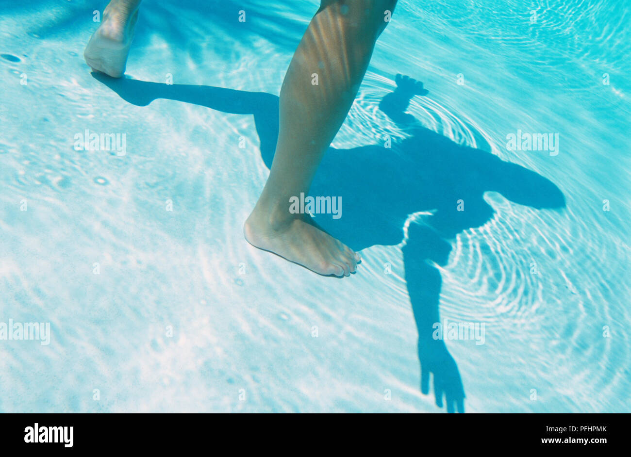 Beine im Wasser des Pools, Schatten des Körpers im Wasser spiegelt. Stockfoto