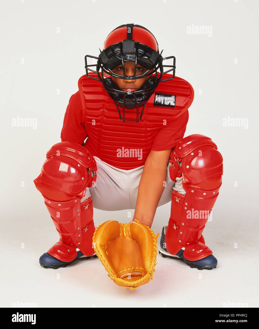 Junge tragen Catcher Ausrüstung, Gesichtsmaske, chest Protector und Bein Guard, kniend mit Grasfangvorrichtungen mit balanciert Stockfoto