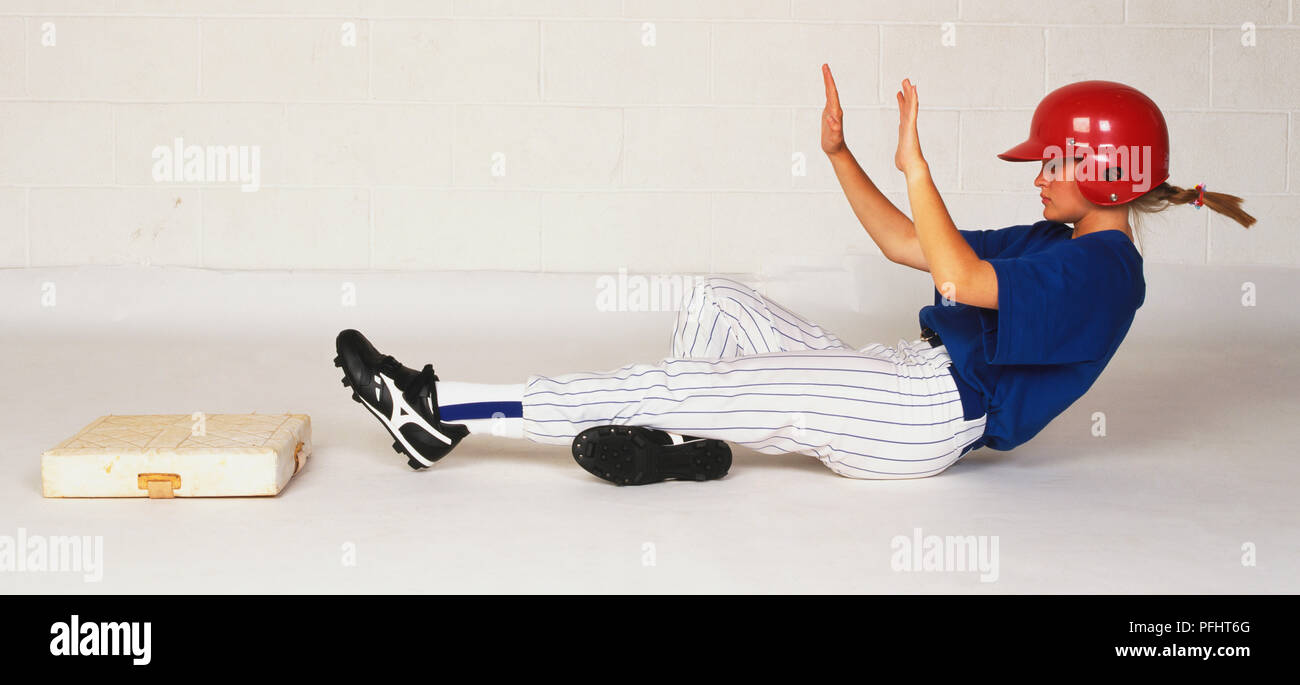 Mädchen im Baseball uniform und Helm gekleidet, Gleiten auf dem Boden, Beine ausgestreckt Infront zur Basis hin Stockfoto