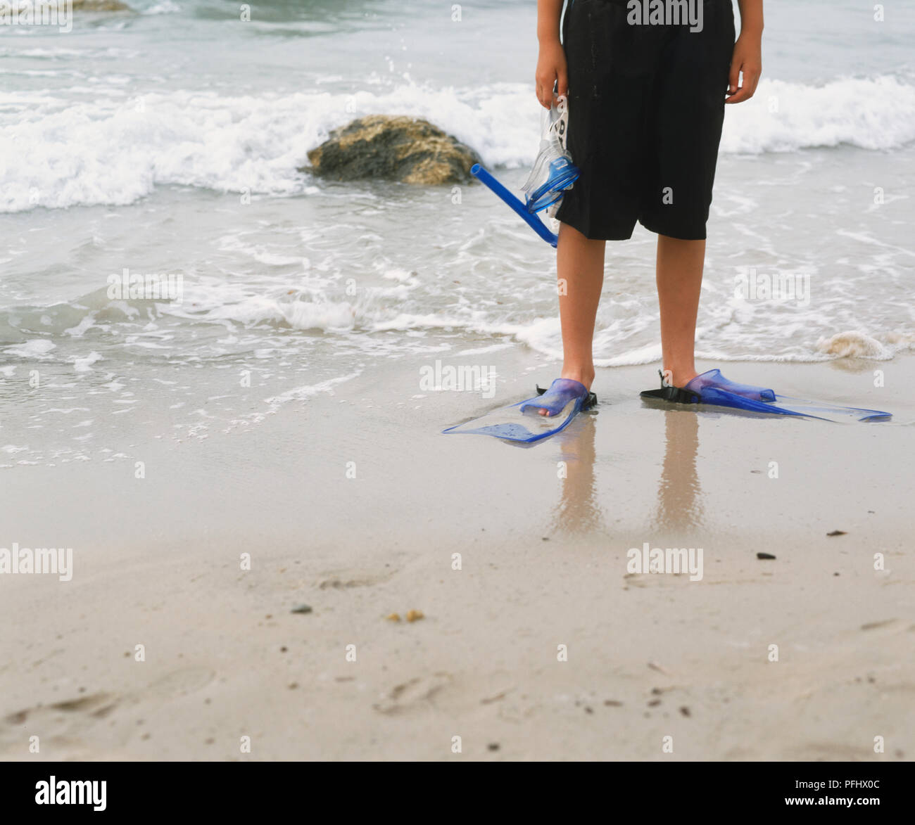 Beine der Junge in Shorts und Kunststoff Flossen, Schnorchel Maske durch Wasser am Strand, Vorderansicht. Stockfoto