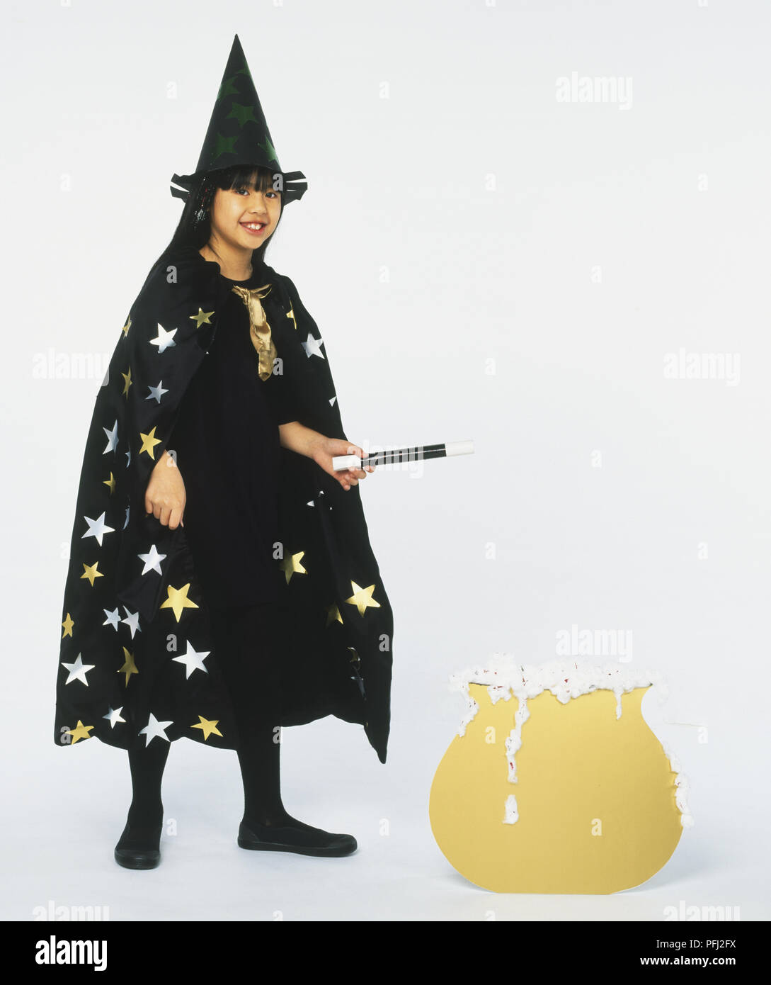 Mädchen gekleidet in Zauberer Umhang und Hut, mit einem Zauberstab, neben Überlaufen pot Stockfoto
