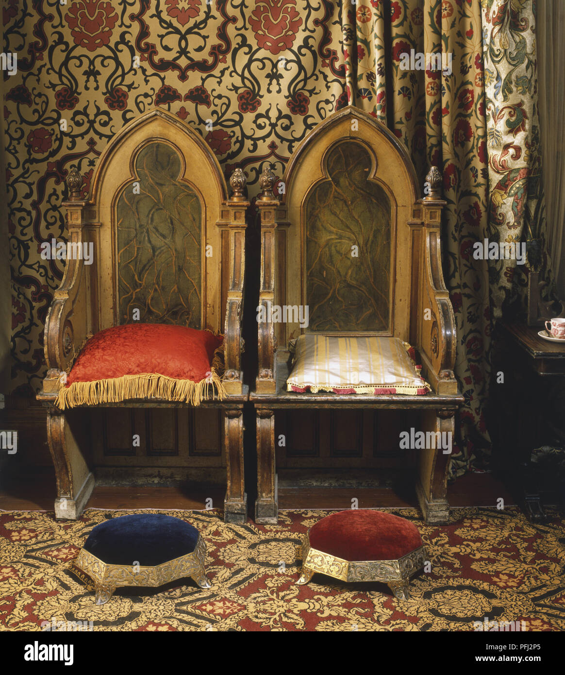 Gotische Interieur mit zwei verzierten Stühle, gepolsterte Schemel und reich gemusterte Vorhänge und Teppich, Vorderansicht Stockfoto
