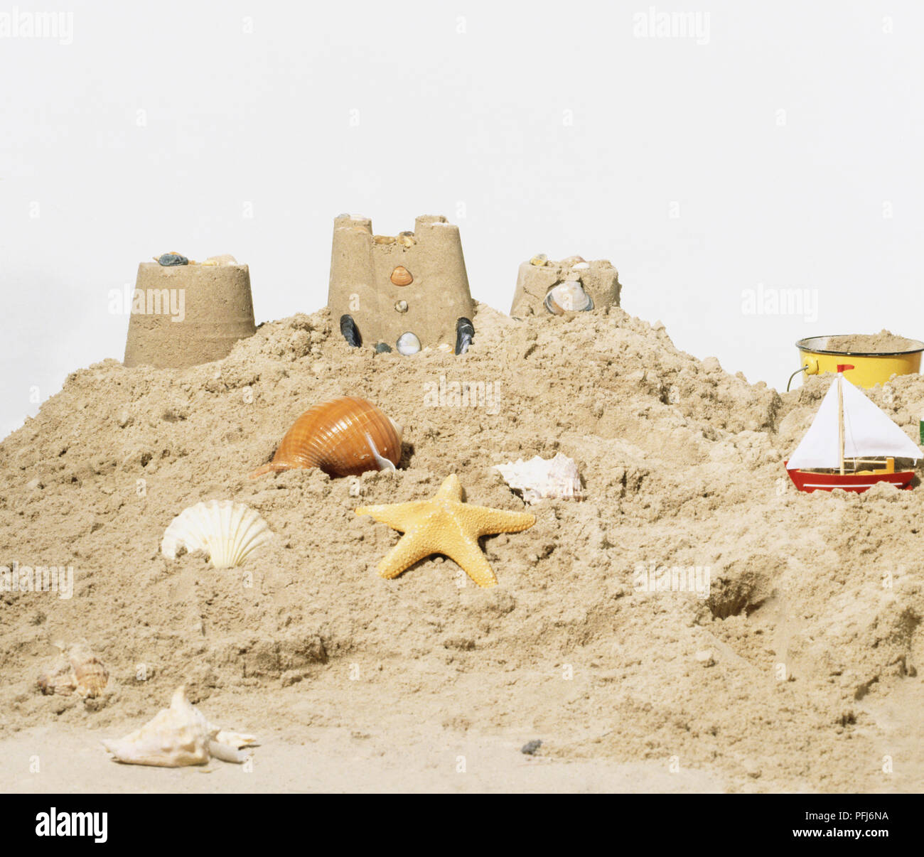 Eimer, Muscheln, Seesterne, Sandcastle und Toy Boat im Sand Stockfoto