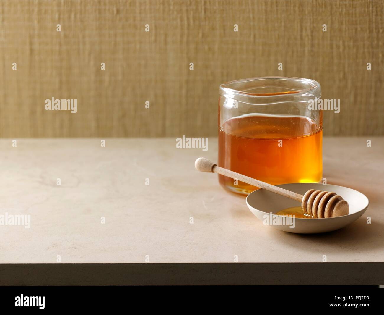 Honig in einem Glas, neben Honig Pendelarm in einer kleinen Schale Stockfoto