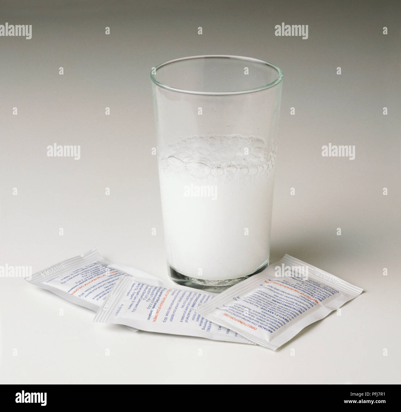 Hoch Klarglas Hälfte mit Weiß fizzy Flüssigkeit und drei identische Sachets mit Gebrauchsanweisung auf der Rückseite ausgefüllt, 'Antazida', 'sanfte Abführmittel", "Erfrischend" trinken und die Warnung "Außer Reichweite von Kindern halten' Stockfoto