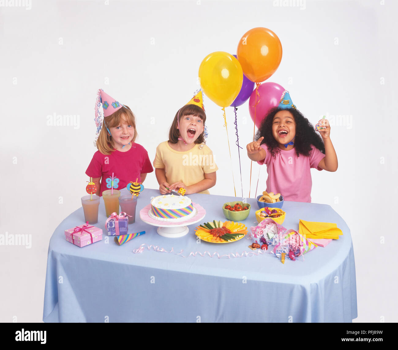 Drei Mädchen in parteihüte lachend und Kamera beim Sitzen am Tisch für Geburtstagsfeier dekoriert, mit Essen und Trinken und Luftballons. Stockfoto